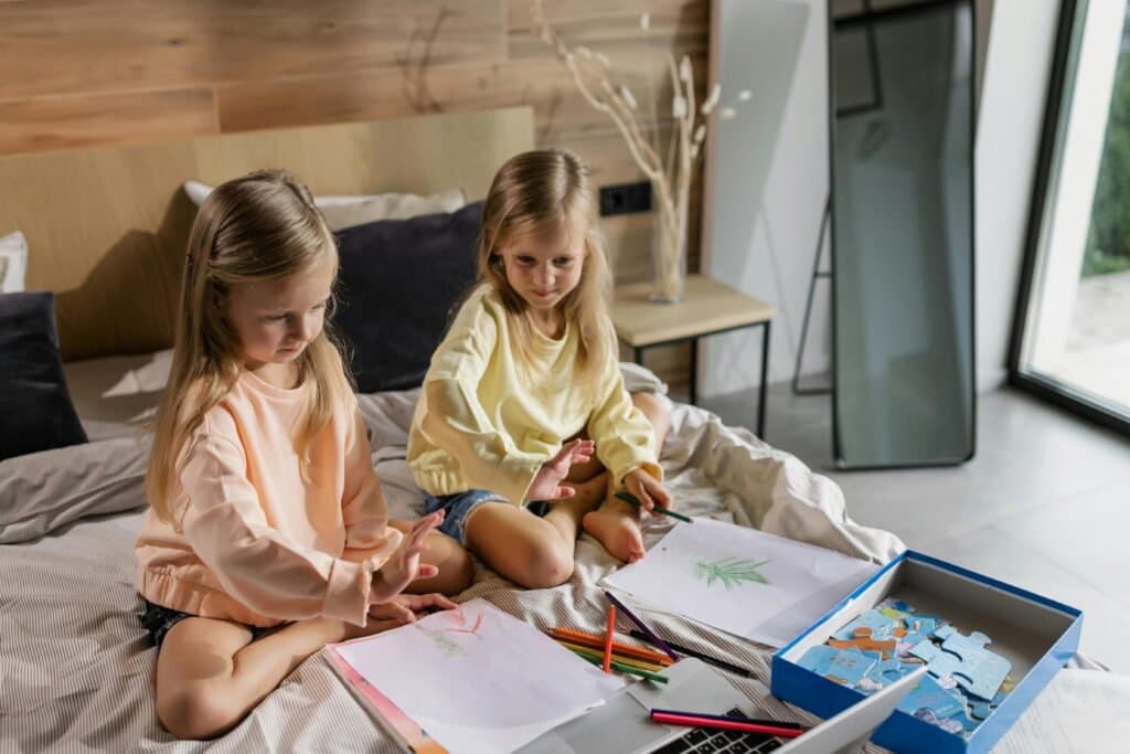 Two teenage twin girls, showing different personalities, engaged in a homeschooling lesson at a desk